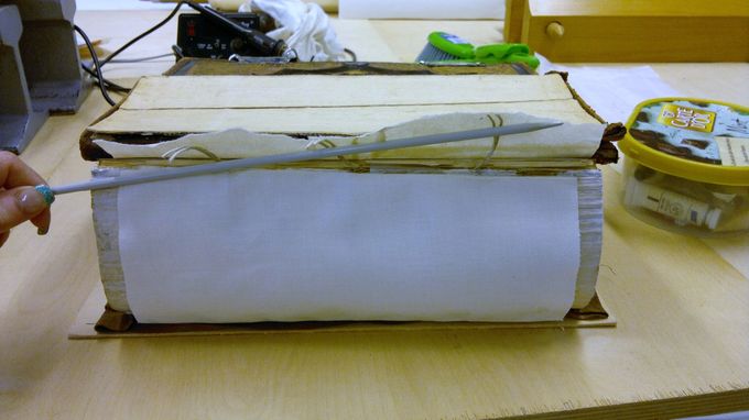 Tässä kuvassa näkyy jatketut bindit ja sidonta-arkki, vahvistettu selkä ja holkki, jonka avulla selkä kiinnitetään sidokseen. Puikko on kuvausrekvisiittaa.